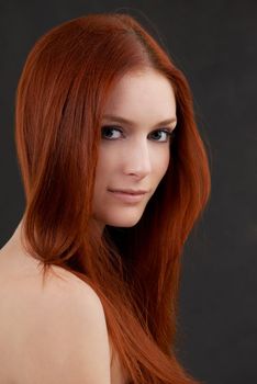 Portrait of a gorgeous young redheaded woman against a black background.