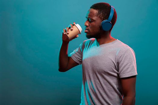 Carefree guy listening to music on headset and drinking coffee