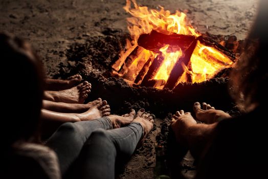 Cropped shot of a group of unrecognizable friends sitting around a bonfire on the beach at night.
