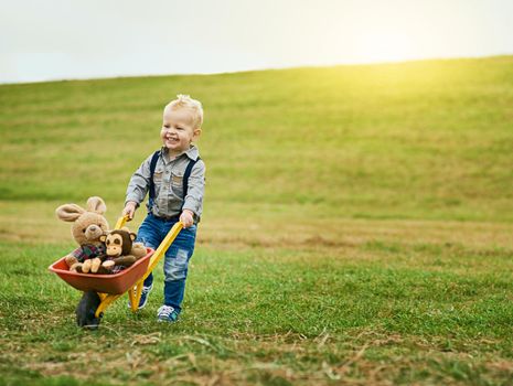 Shot of an adorable little boy pushing a toy wheelbarrow filled with stuffed animals on a farm.
