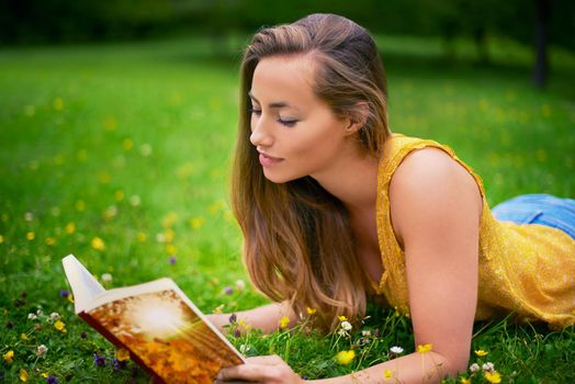 Reading a spellbinding story. Shot of a carefree young woman relaxing in a field of grass with a book.