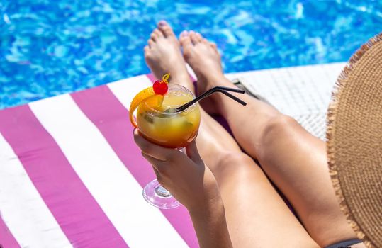 a girl on a sun lounger near the pool drinks a cocktail from a freshly squeezed orange. Recreation