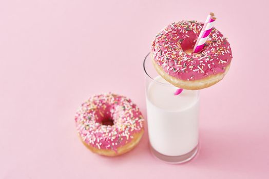 Donuts decorated with icing and sprinkle and glass of milk on a pink background