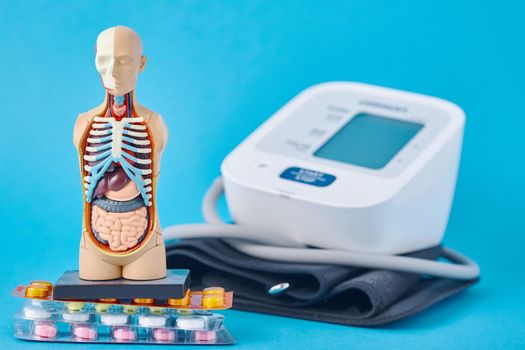Digital blood pressure monitor, anatomical dummy man mannequin and medical pills on blue background. Healthcare and medicine concept