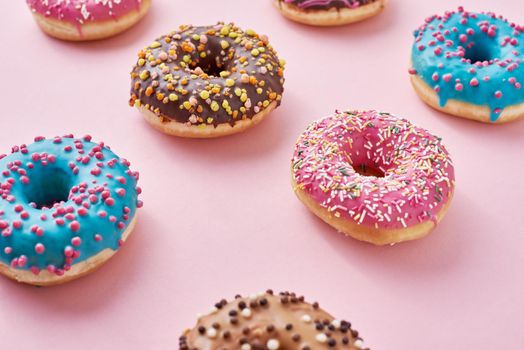 Pattern with different types of colorful donats decorated sprinkles and icing on a pastel pink background, top view flat lay