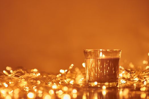 Burning candle with a golden garland lights in bokeh on dark background