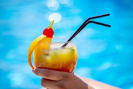 a girl on a sun lounger near the pool drinks a cocktail from a freshly squeezed orange. Recreation