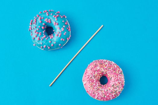 Two donuts separated with a drinking straw on blue background. Creative food concept