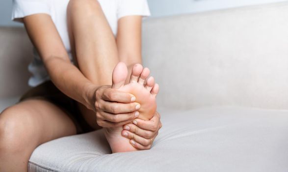Asian woman sitting on sofa feeling pain in her foot at home