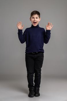 Nice schoolboy is posing at studio over a gray background.
