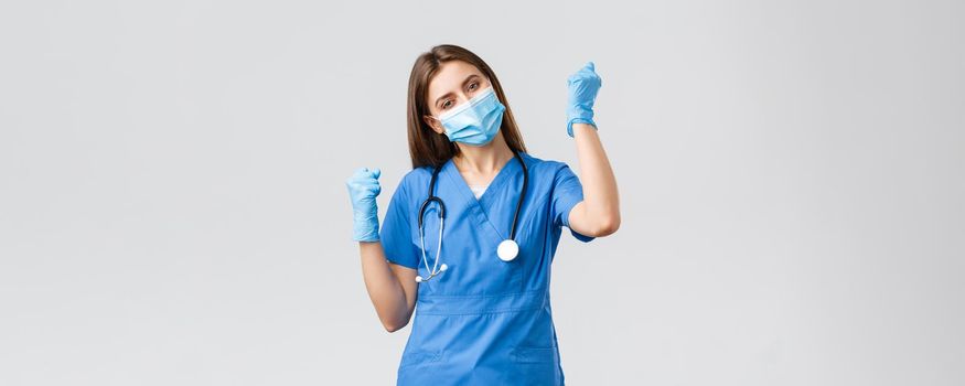 Covid-19, preventing virus, health, healthcare workers and quarantine concept. Cheerful optimistic female nurse winning, celebrating victory, fist pump upbeat, smiling in medical mask and gloves.