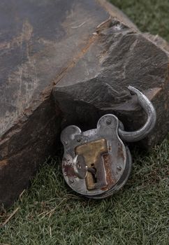 Old vintage iron padlock front of Huge stone on grass background. 