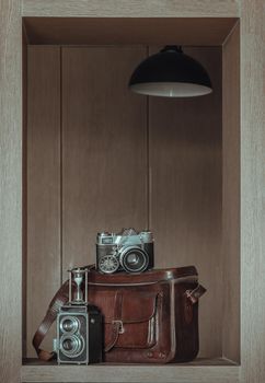 Hourglass on Vintage two lens photo camera, Retro pocket watch, Old vintage film photo camera on Vintage brown leather bag in Square wooden frame Interior. Retro style toned concept design,