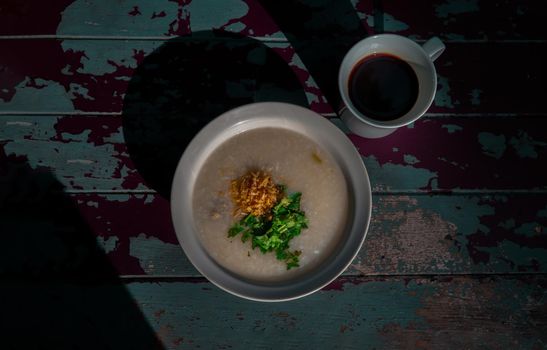 Pork congee or Rice porridge with minced pork sprinkled with deep-fried garlic and coriander in white bowl Served with cup of black coffee.