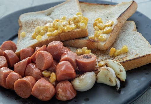 Close-up of breakfast with Fried sausages, Breads, Sweet corn kernels and Garlic.