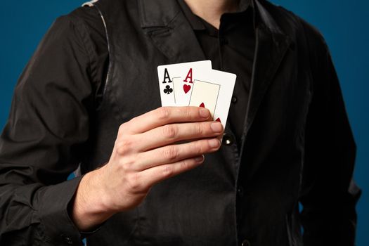 Newbie in poker, in black vest and shirt. Holding two playing cards while posing against blue studio background. Gambling, casino. Close-up.