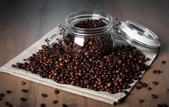 Glass jar with roasted coffee beans on pile of beans