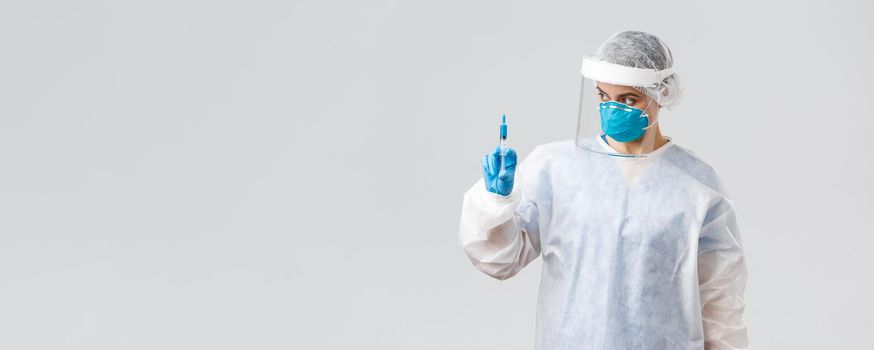 Covid-19, medical research, diagnosis, healthcare workers and quarantine concept. Professional doctor in personal protective equipment, PPE costume, holding syringe with coronavirus vaccine