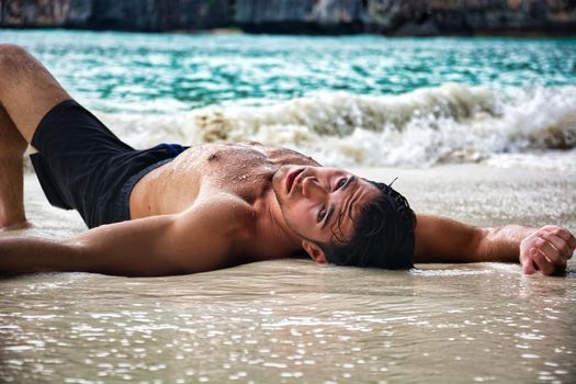 Shirtless young man on the beach lying on sand