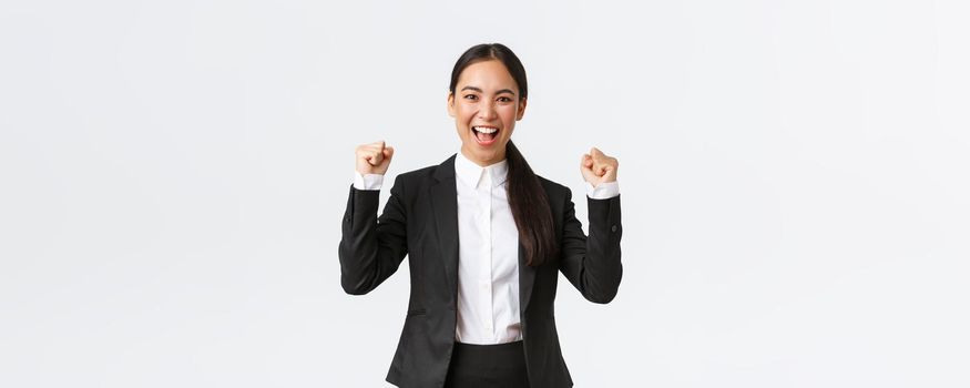 Successful winning female entrepreneur in black suit, fist pump and shouting yes excited, celebrating victory. Businesswoman triumphing over big achievement over white background