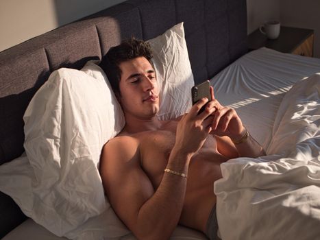 Handsome young man in bed typing on cell phone