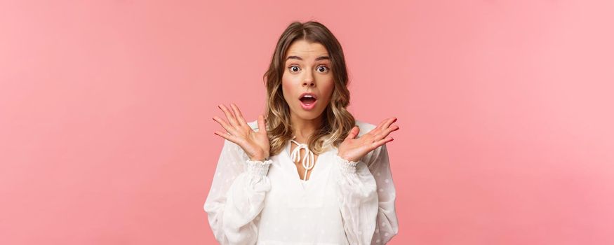 Close-up portrait of impressed and surprised blond girl hear something stunning and impressive happened, drop jaw spread hands sideways, look astonished with news, pink background