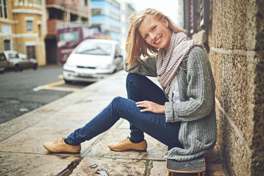 Full length portrait of an attractive young woman sitting on her skateboard in the city.
