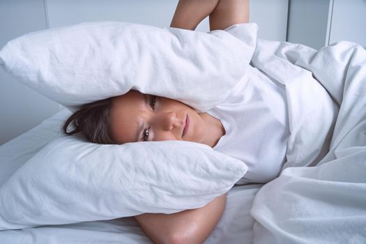 Young woman can't sleep because of noisy neighbours and covering ears with pillows