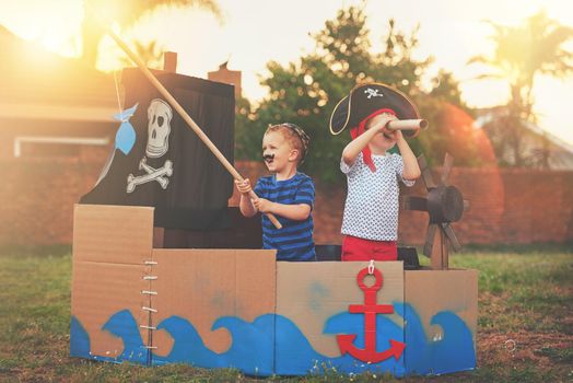 These little pirates just want to have fun. Shot of a cute little boy and his brother playing pirates outside on a boat made of cardboard boxes.