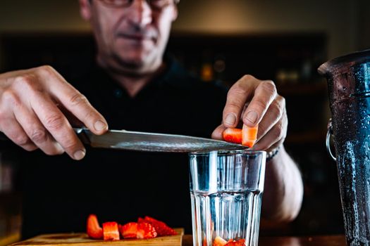hands of an experienced bartender pouring fruit into a glass cocktail glass. Cocktail preparation in a nightclub.