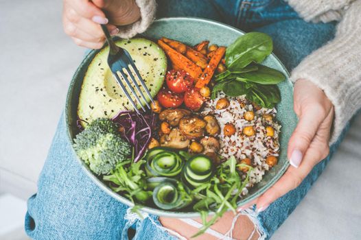 Woman eating healthy meal. Bowl with rice, quinoa, avocado, cucumber, broccoli and cucumber. Healthy diet, lunch or dinner. Healthy food plate