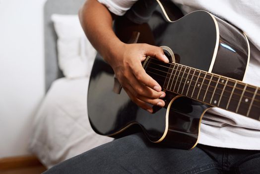 Its a great way to express yourself. Shot of a young man playing the guitar while sitting at home.