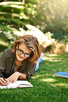 Putting it in her diary. Shot of an attractive young woman writing in her diary while outside on the grass.