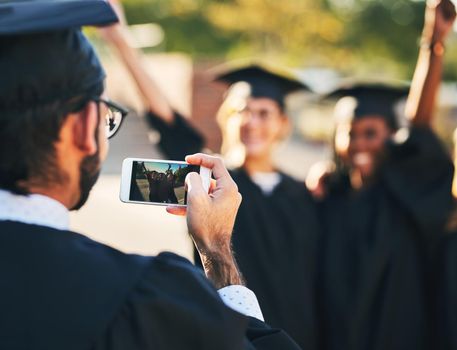 Memories from the big day. Shot of a group of students taking pictures with a mobile phone on graduation day.