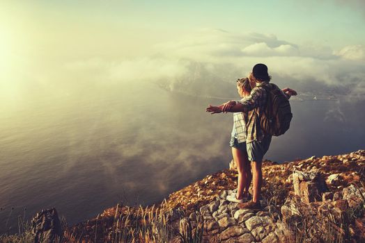 Lets fly away together. Shot of an adventurous young couple admiring the view from a mountain peak while out on a hike.