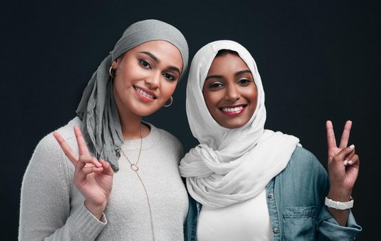 Millennial trends. Cropped shot of two attractive young women wearing hijabs and standing together while showing a peace sign in the studio.