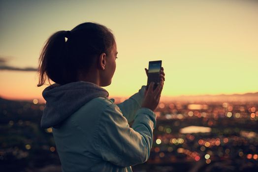 Theres always time for a photo. Rearview shot of a young woman sending a text message while standing on a lookout point.