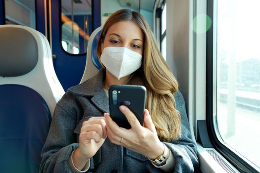 Relaxed woman with KN95 FFP2 face mask using smart phone app. Train passenger with protective mask traveling sitting texting on mobile phone. Travel safely on public transport.