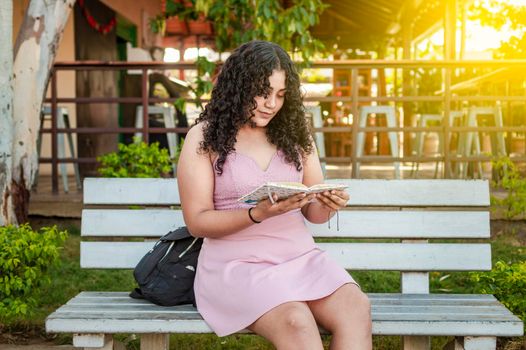 A cute girl sitting on a bench reading a book, pretty young latin girl reading a book on a bench