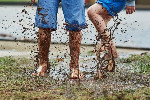 Be young, make a mess. Low angle shot of two unrecognizable children jumping around in mud outside during a rainy day.