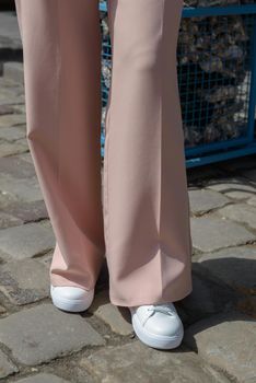 Stylish woman in fashion white sneakers shoes and beige trousers walks around the city.