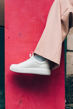 Stylish woman in fashion white sneakers shoes and beige trousers. pink background.