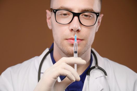 Studio portrait of a male doctor in a white coat with a syringe and an ampoule of a vaccine in his hands. Caucasian doctor on brown background