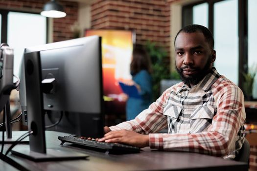 African american creative company employee sitting at desk in office workspace while looking at camera.