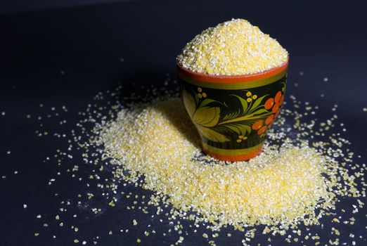 Raw bright yellow corn grits flour in a wooden bowl on a black background