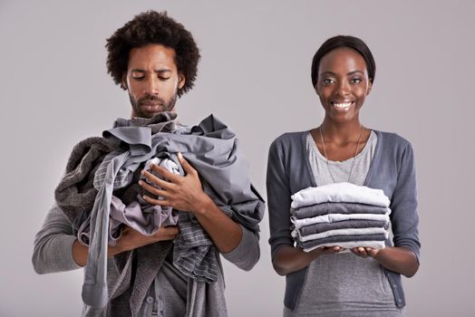 Men are from Mars.... Studio shot of a woman holding a neatly folded pile of clothes while her partners is in a mess.