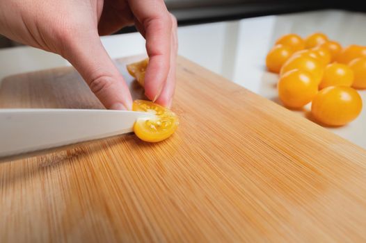 Sliced yellow cherry tomatoes on a wooden board in shallow depth of field against the background of a bowl with veggie salad ingredients