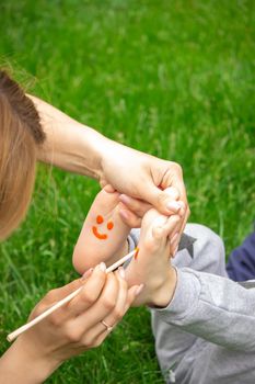 child sitting on the grass, smiling on the child's leg with paints, selective focus