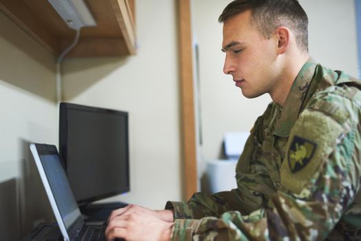 Army life, its not all guns and grenades. Shot of a young soldier using a laptop in the dorms of a military academy.