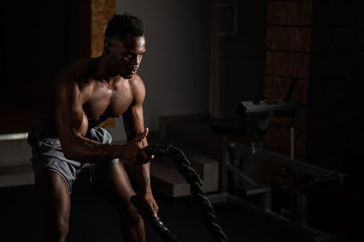 Attractive african american man with naked torso doing endurance exercises with trope.